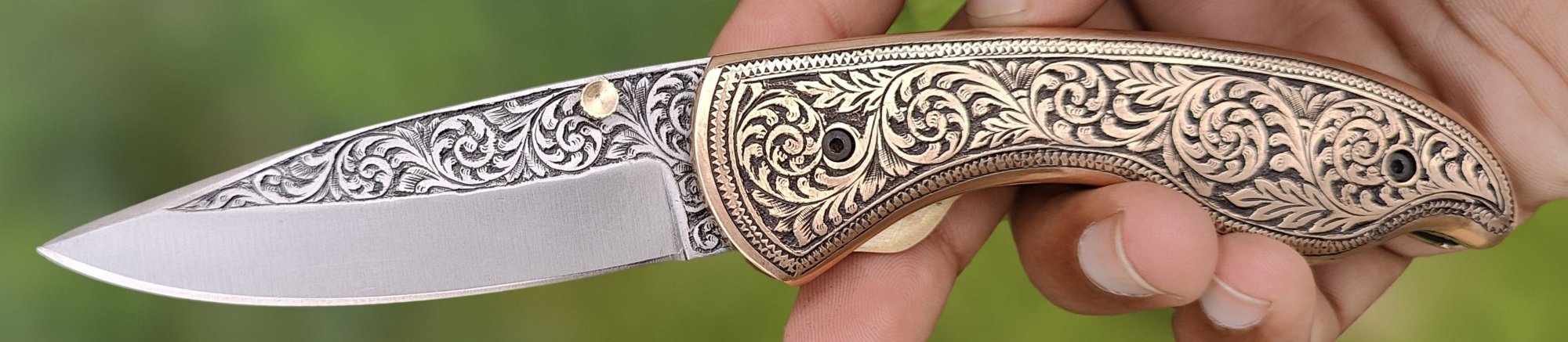 Folding pocket knife with a hand engraved blade and brass scrollwork handle, open