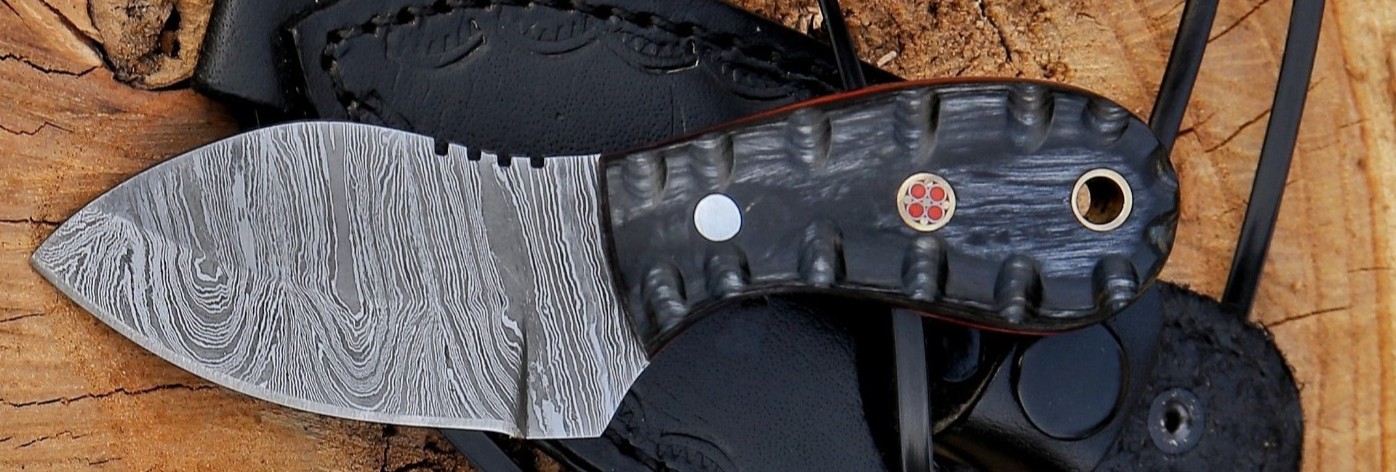 Damascus neck knife with a textured black handle, red mosaic pin and brass lanyard hole, resting on a leather sheath