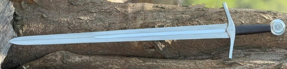 Medieval arming sword with a tapering double edged blade, straight crossguard and a round pommel, resting on a log